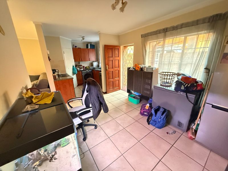 Open plan living and kitchen area featuring tiled flooring, wooden cabinetry, and direct access to an outdoor space via a security gate.