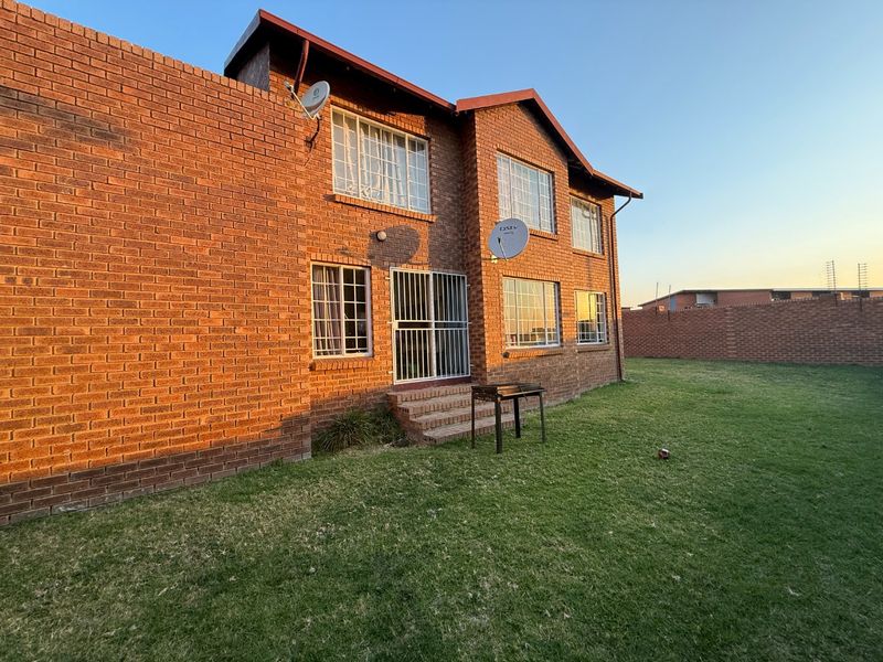 Rear view of a double-story face brick apartment building featuring a private lawn area and secure access point.