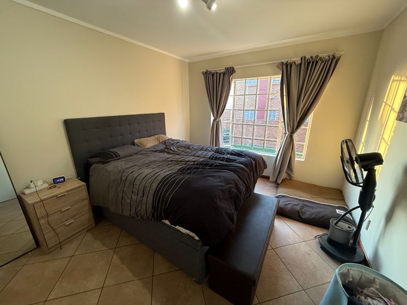 A bedroom featuring tiled flooring and a large window with security bars, providing natural light.