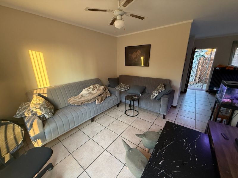 A living room featuring ceramic floor tiles and a ceiling fan, with an open transition to an exterior entrance area.