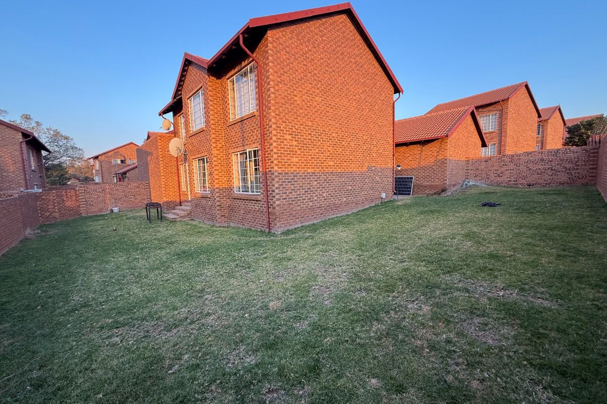 A view of the rear exterior of the apartment building, featuring face brick construction, a tiled roof, and a private grassed garden area.