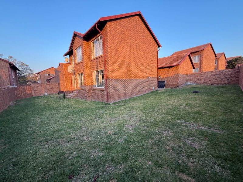 A view of the rear exterior of the apartment building, featuring face brick construction, a tiled roof, and a private grassed garden area.