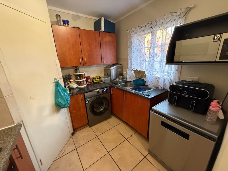 Compact kitchen featuring laminate cabinetry, stone-look countertops, stainless steel sink, and integrated space for a washing machine with tiled flooring.
