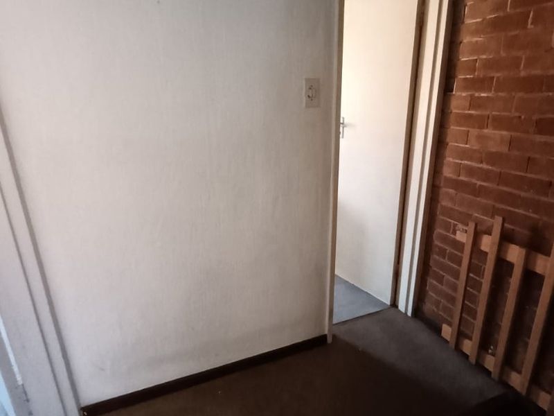 A simple hallway featuring an exposed brick wall and carpeted flooring, leading to an adjacent room.