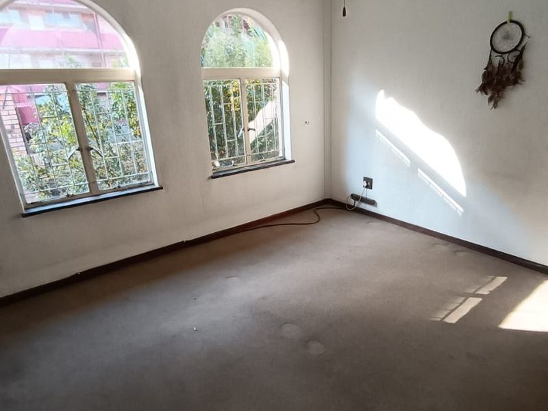 An empty bedroom featuring arched windows with security bars, a ceiling fan, and carpeted flooring.