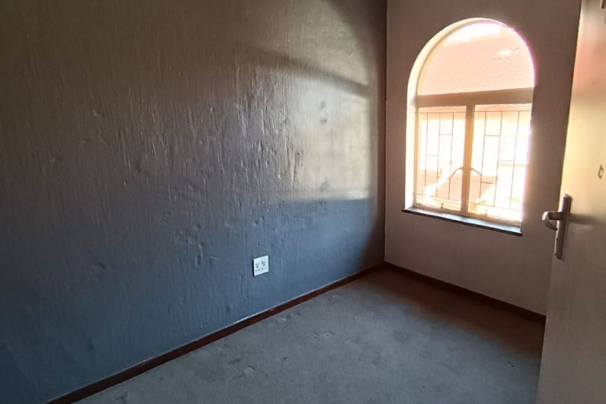 An empty bedroom featuring a ceiling fan, arched window with security bars, and grey carpet flooring.