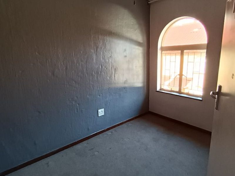 An empty bedroom featuring a ceiling fan, arched window with security bars, and grey carpet flooring.