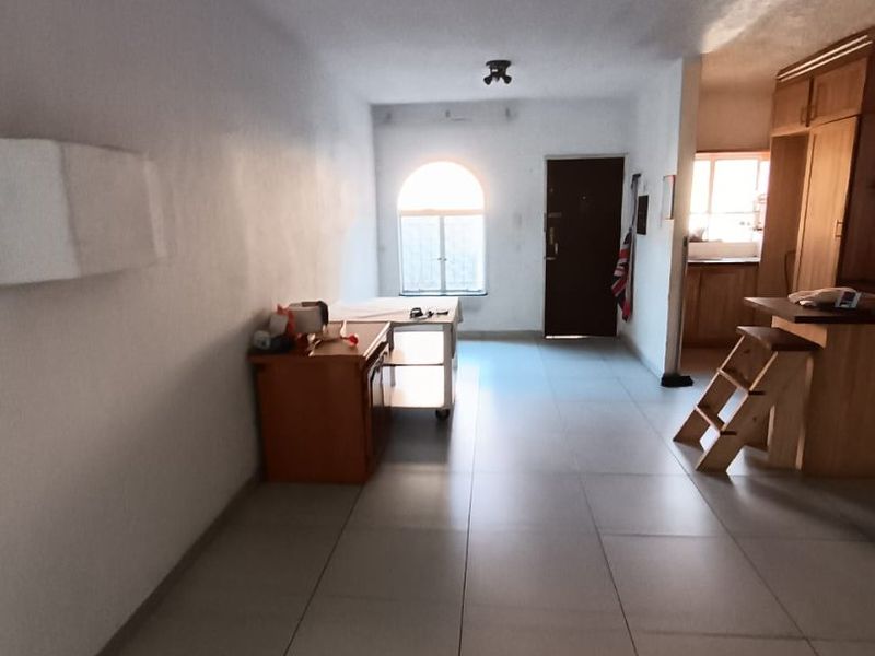 Open-plan living area featuring tiled flooring, an arched window, and an adjoining kitchen space with built-in cabinetry and a breakfast counter.