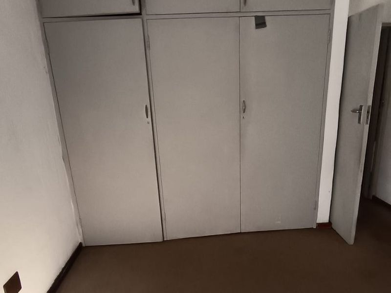 A bedroom featuring built-in cupboards with overhead storage and carpeted flooring, presenting a dated aesthetic in need of cosmetic updates.