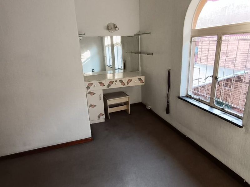 Bedroom featuring a built-in vanity unit, arched window with security bars, and carpeted flooring.