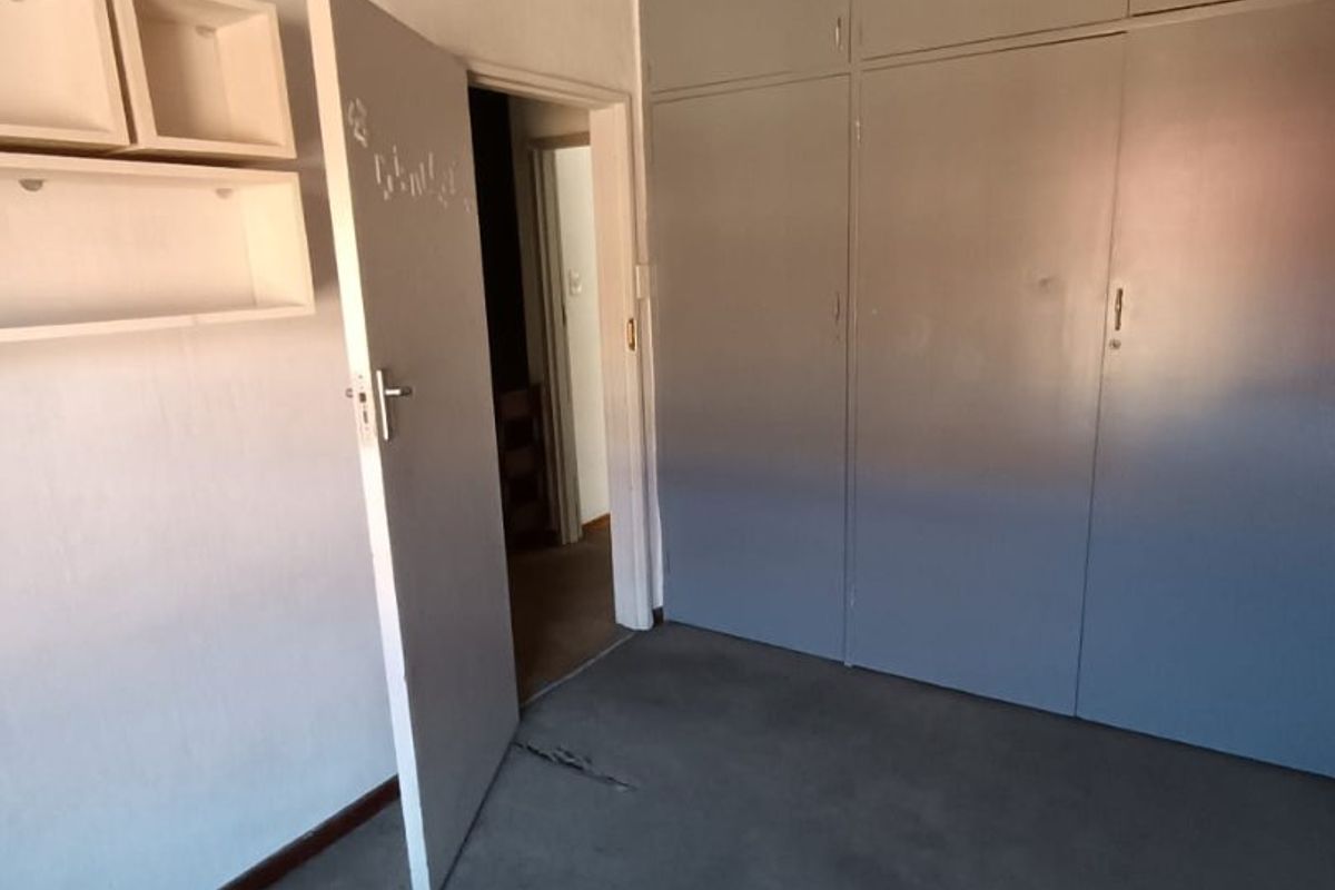 A vacant bedroom featuring built-in cupboards, a ceiling fan, and carpeted flooring, offering a blank canvas for potential updates and modernization.
