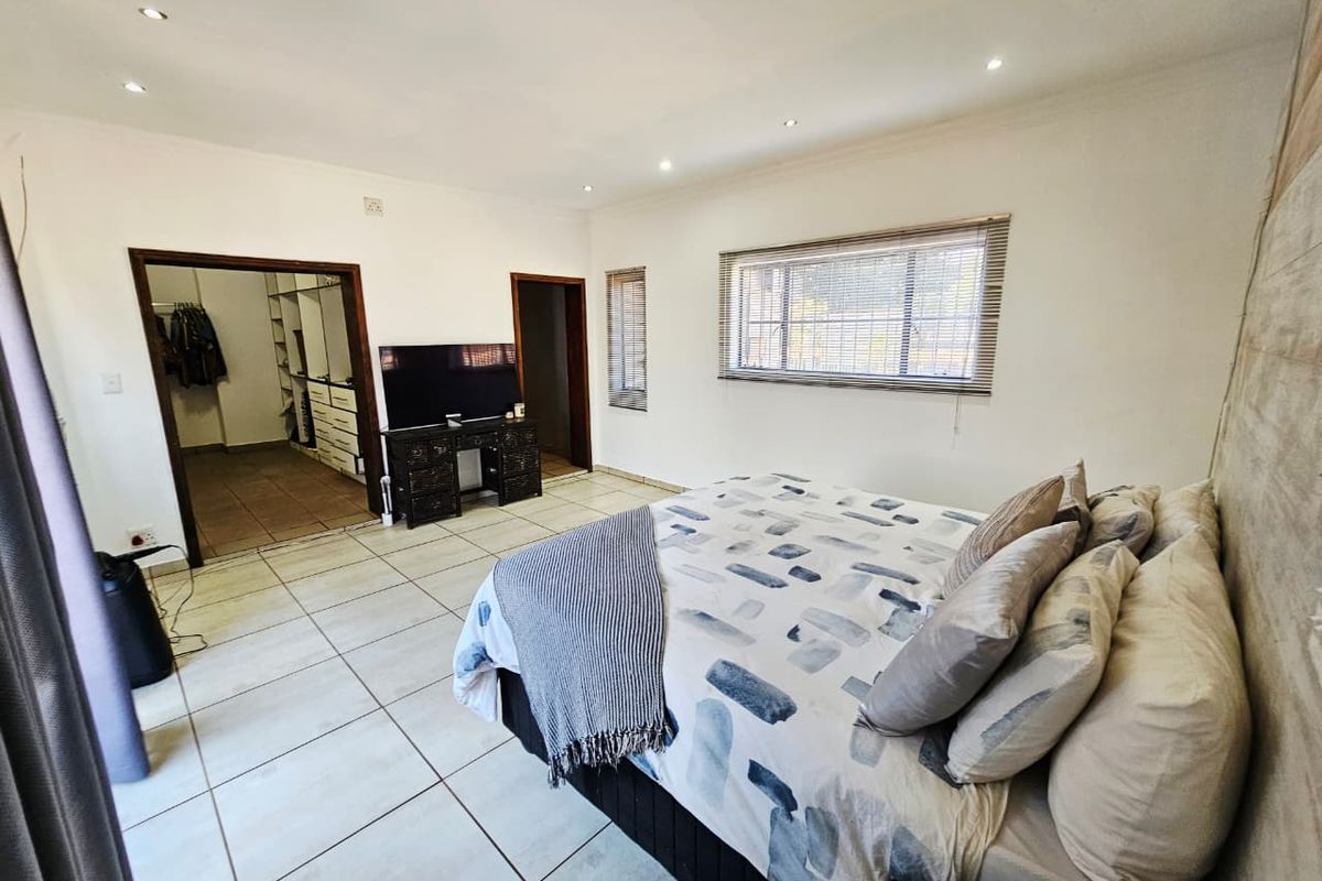 Spacious bedroom featuring tiled flooring, recessed downlights, and an adjoining walk-in closet area with built-in storage.