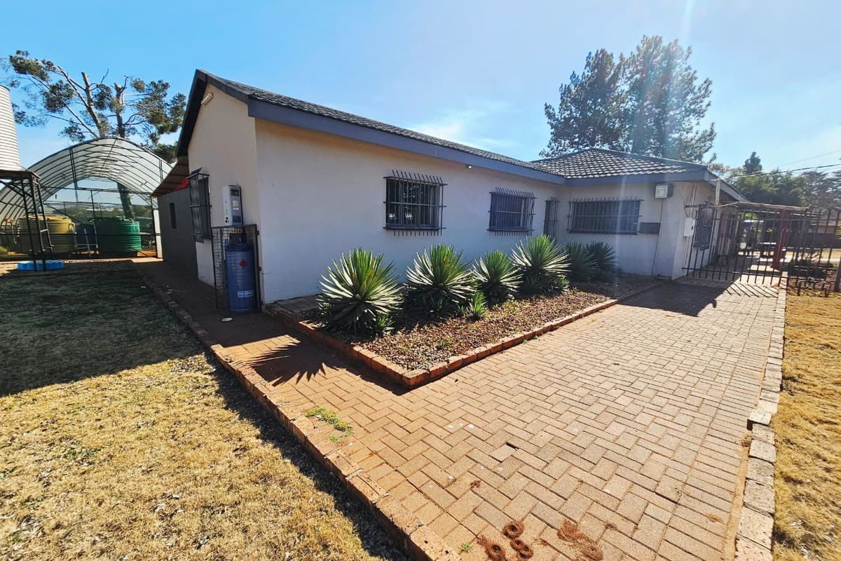 Rear exterior view of the house featuring a paved patio area, security bars on windows, and a tiled roof.