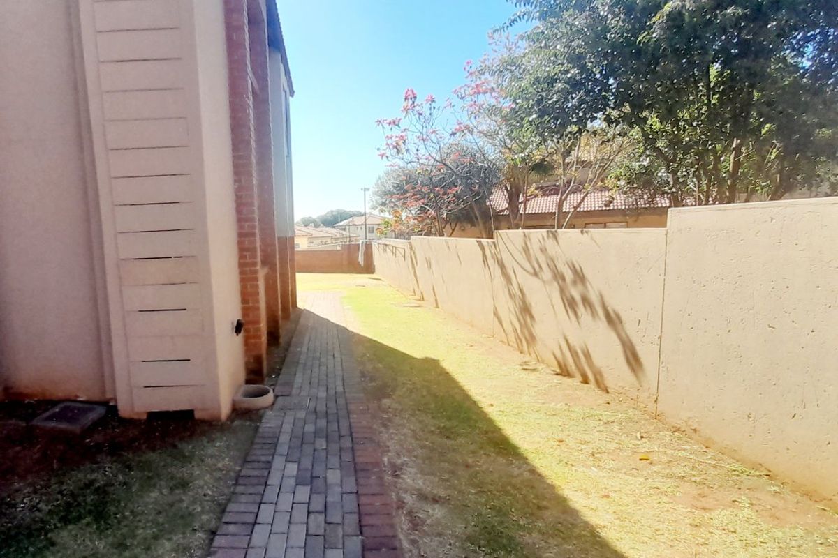 A side walkway featuring paved brick pathways running alongside the building exterior and a high boundary wall.