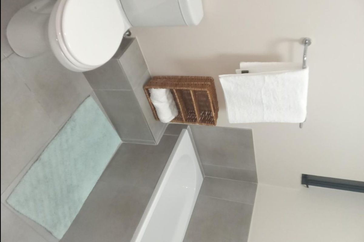 A clean, modern bathroom featuring a bathtub, toilet, and neutral grey wall and floor tiling.