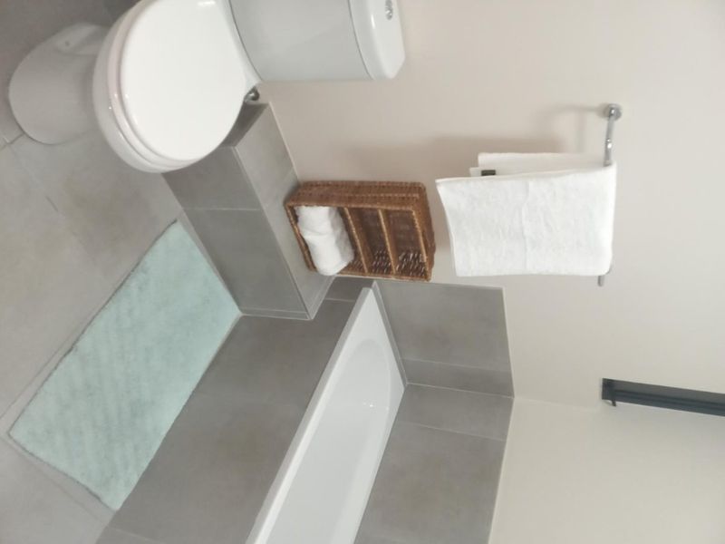 A clean, modern bathroom featuring a bathtub, toilet, and neutral grey wall and floor tiling.