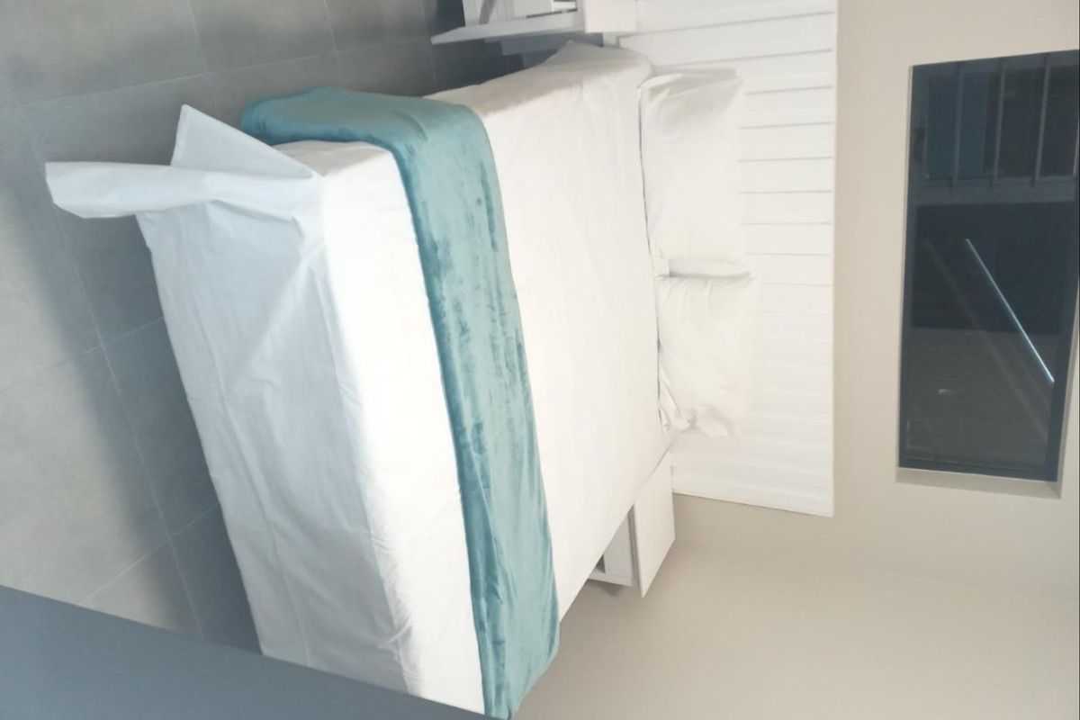 A modern bedroom featuring a built-in white headboard and neutral tiled flooring, presented in a clean and minimalist style.