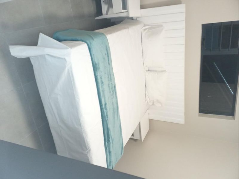 A modern bedroom featuring a built-in white headboard and neutral tiled flooring, presented in a clean and minimalist style.