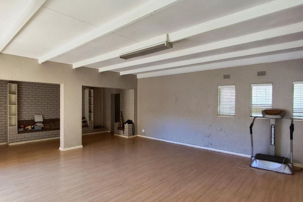 Spacious living area featuring exposed beam ceilings, laminate flooring, and built-in shelving units, offering a versatile open-plan layout.