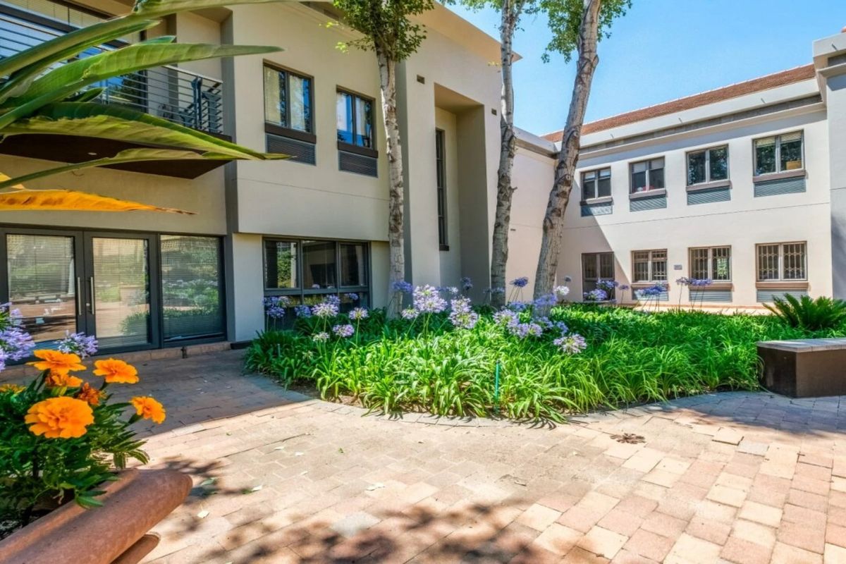 A well-maintained commercial courtyard featuring paved walkways, landscaped garden beds, and multi-story building facades with balconies and secure window treatments.