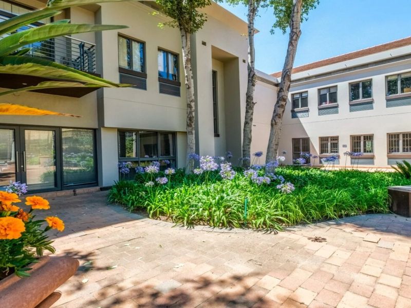 A well-maintained commercial courtyard featuring paved walkways, landscaped garden beds, and multi-story building facades with balconies and secure window treatments.