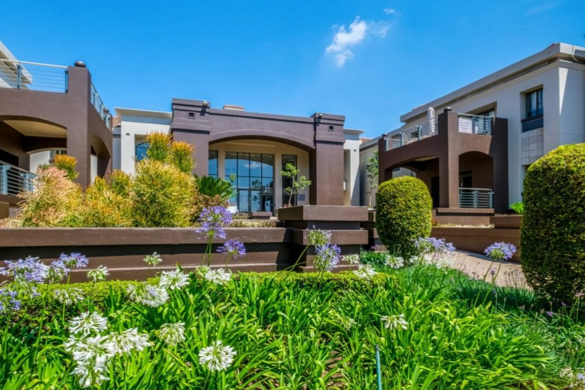 A well-maintained commercial building exterior featuring landscaped gardens, modern stucco facade, and covered balconies with glass railings.