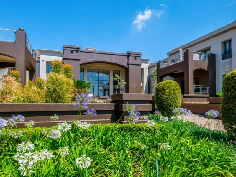 A well-maintained commercial building exterior featuring landscaped gardens, modern stucco facade, and covered balconies with glass railings.