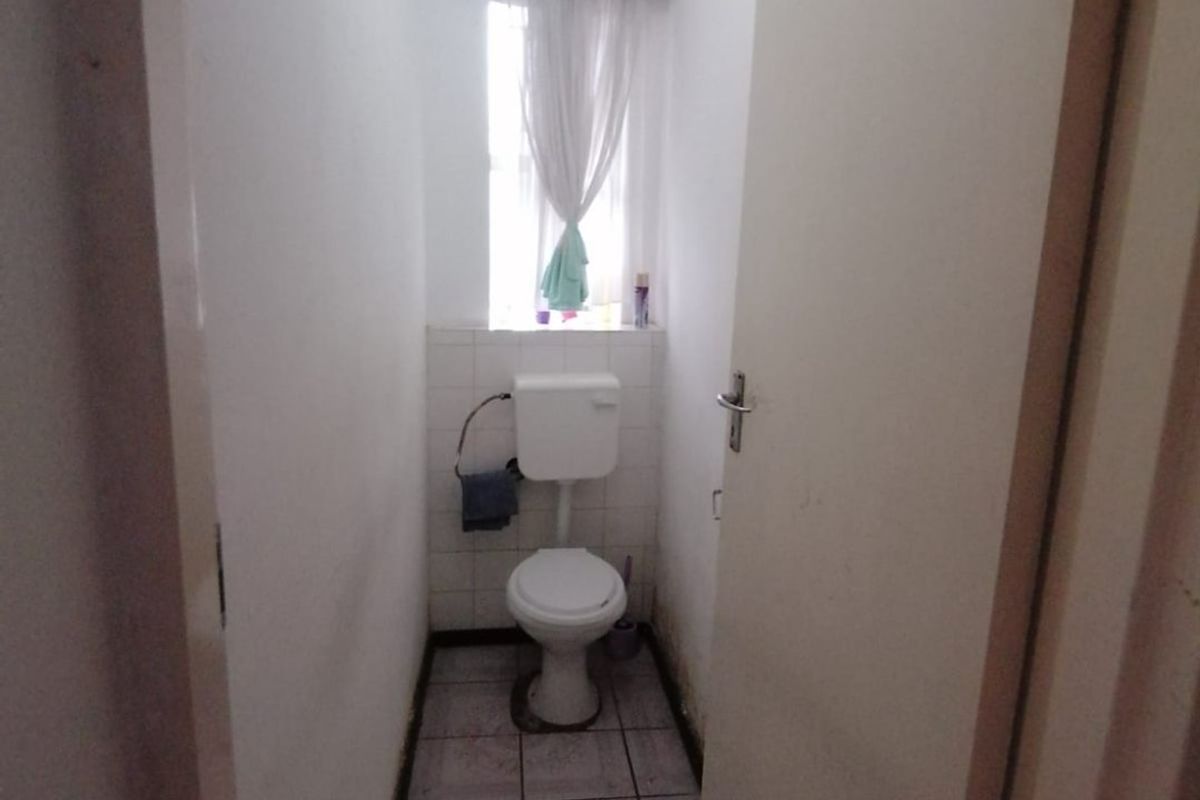 A compact, functional guest toilet featuring tiled flooring and a window, currently in need of cosmetic updates to improve its overall condition.