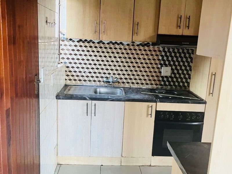 Compact kitchen featuring built-in cabinetry, integrated oven and hob, tiled splashback, and tiled flooring. Requires minor ceiling repairs and cosmetic updates.