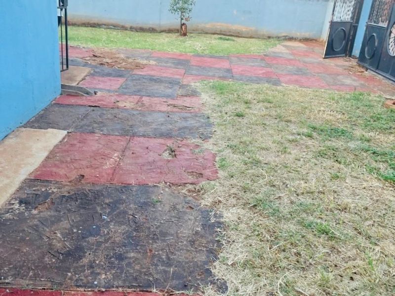 A rear garden area featuring a perimeter wall, metal gate, and a paved patio section in need of maintenance and landscaping.