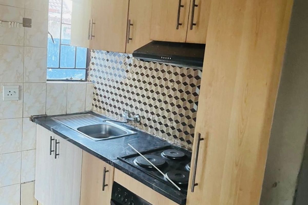 Compact kitchen featuring light wood-tone cabinetry, dark laminate countertops, built-in oven with electric hob, and a decorative tiled backsplash.