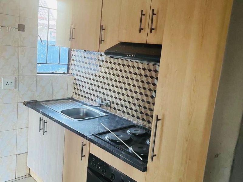Compact kitchen featuring light wood-tone cabinetry, dark laminate countertops, built-in oven with electric hob, and a decorative tiled backsplash.