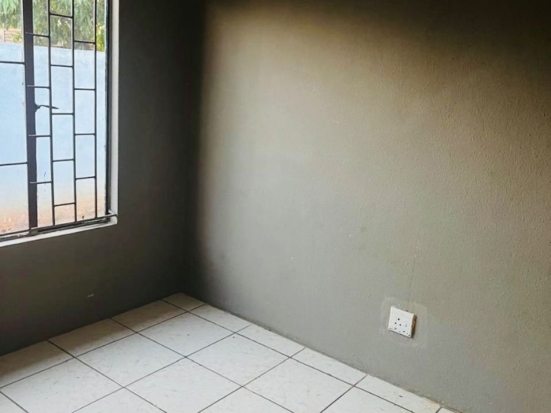 An empty bedroom featuring tiled flooring, dark painted walls, and a window fitted with security bars.