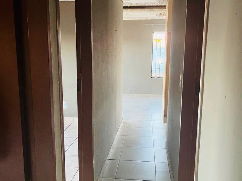 A narrow hallway featuring tiled flooring and decorative ceiling cornicing, leading into adjacent rooms. The space requires cosmetic updates to the ceiling and walls.