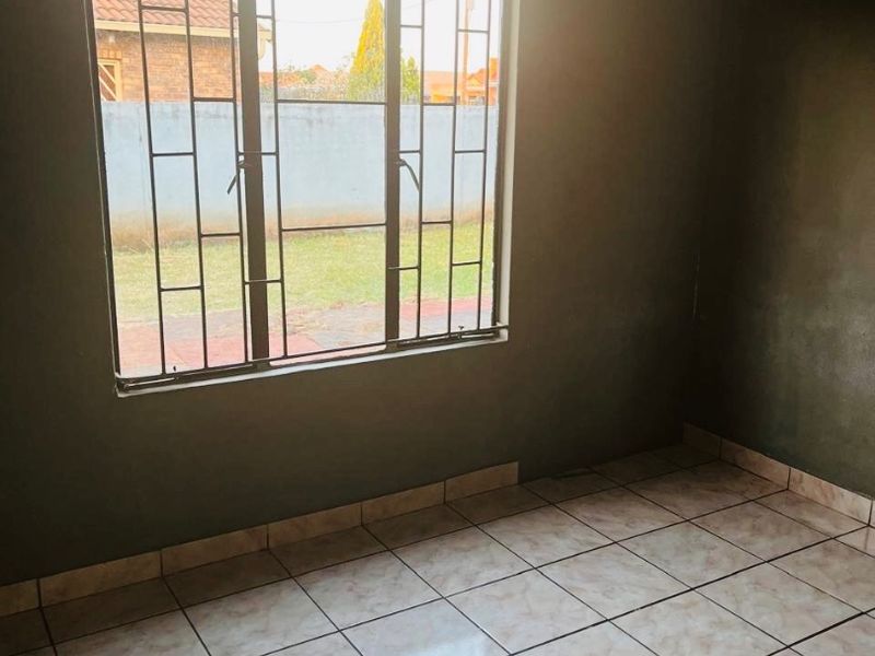 An empty bedroom featuring tiled flooring and security bars on the window, offering a blank canvas for potential interior updates.