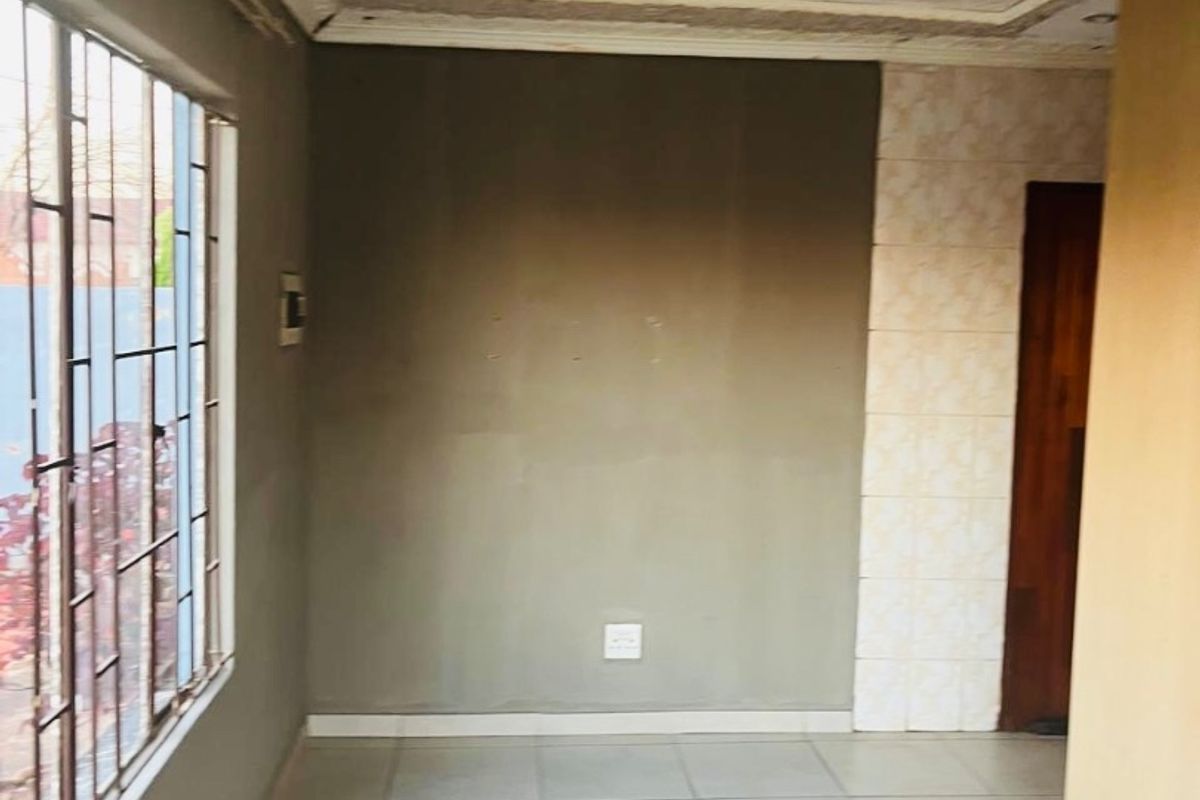An empty living area featuring tiled flooring, security bars on the window, and decorative ceiling detailing with recessed lighting.