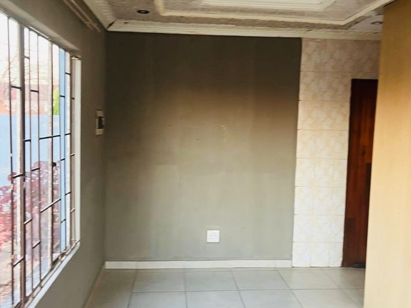 An empty living area featuring tiled flooring, security bars on the window, and decorative ceiling detailing with recessed lighting.