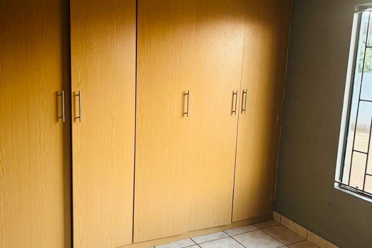 A bedroom featuring built-in wooden wardrobes, tiled flooring, and a window with security bars.