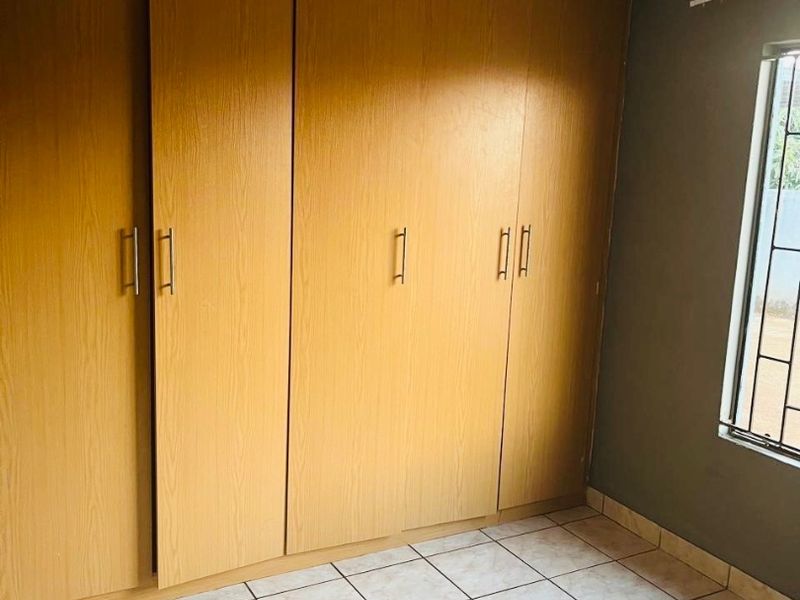 A bedroom featuring built-in wooden wardrobes, tiled flooring, and a window with security bars.