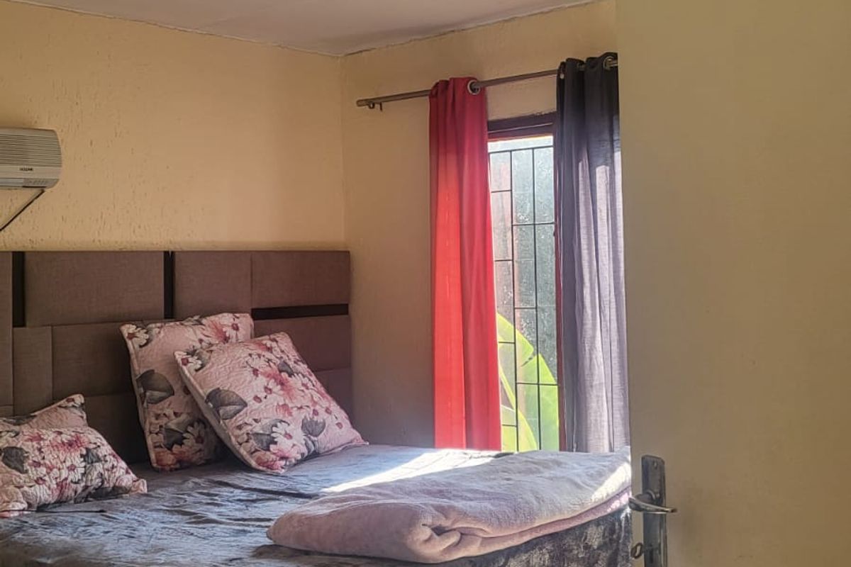 A bedroom featuring tiled flooring, an installed air conditioning unit, and a window fitted with a security gate.