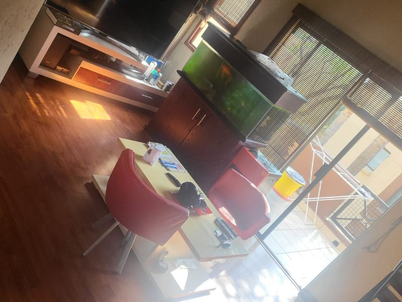 A living room area featuring laminate flooring and large sliding glass doors with venetian blinds, providing access to an outdoor balcony space.