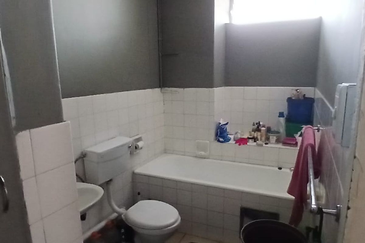A functional bathroom featuring a standard bathtub, toilet, and washbasin with tiled finishes, requiring cosmetic updates to improve its overall condition.