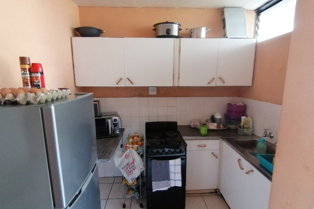 Compact kitchen featuring white cabinetry, tiled backsplash, stainless steel sink, and a freestanding stove, offering a functional layout with potential for modernization.