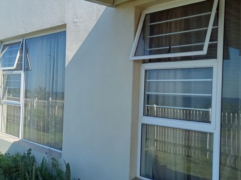 Exterior view of the apartment building facade featuring white painted walls and aluminium framed windows with security bars.