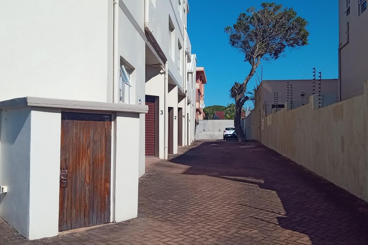 Rear exterior view of the apartment complex featuring a paved driveway, perimeter wall with electric fencing, and access to storage units.