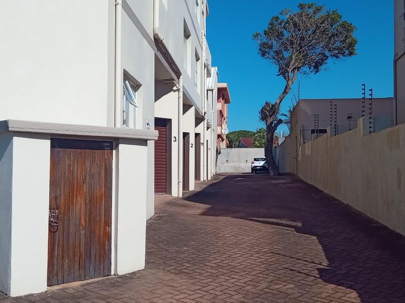 Rear exterior view of the apartment complex featuring a paved driveway, perimeter wall with electric fencing, and access to storage units.