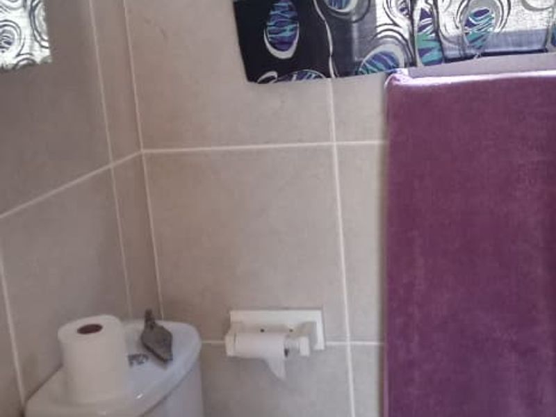 A functional bathroom featuring a pedestal basin, toilet, and neutral ceramic wall and floor tiling.