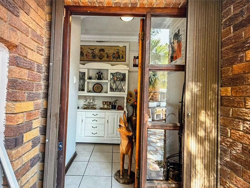 View through a timber-framed glass door into an entrance hall featuring tiled flooring and exposed brick exterior detailing.
