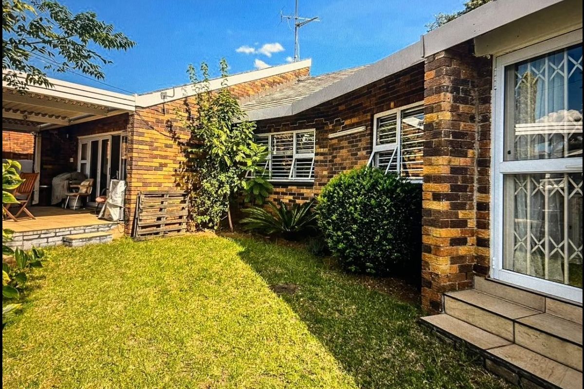 Rear view of the property featuring a brick facade, a covered patio area, and a well-maintained garden lawn.