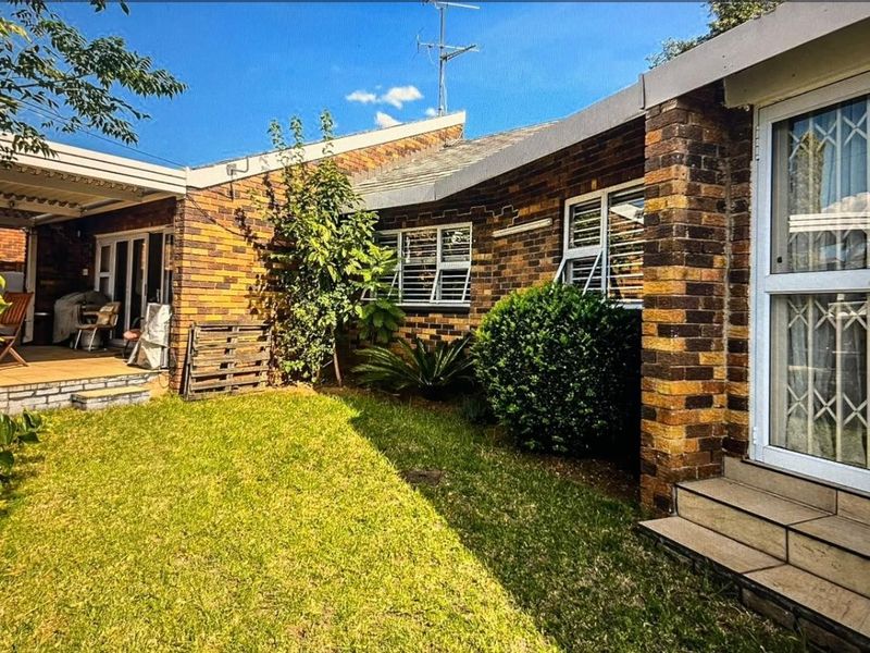 Rear view of the property featuring a brick facade, a covered patio area, and a well-maintained garden lawn.